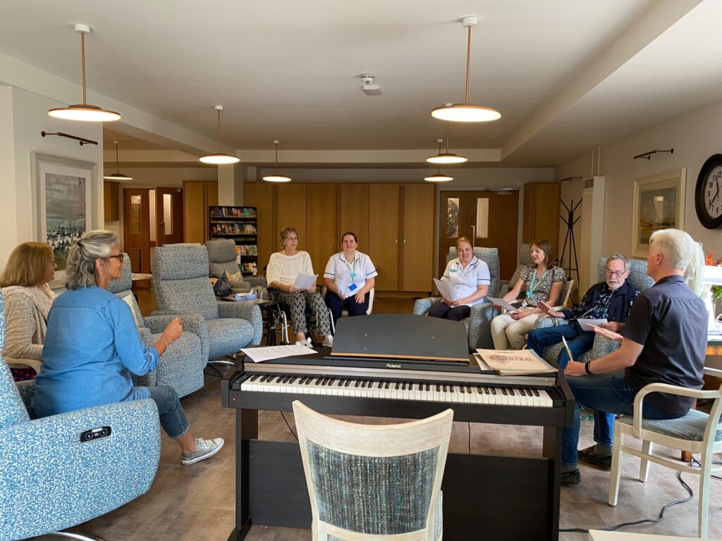 A group of people seated in the Living Well Centre with two volunteers leading the group