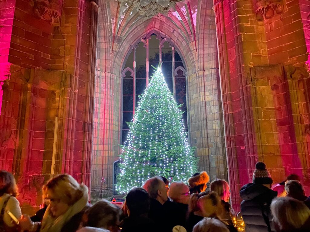 People gather around an illuminated Christmas tree which features lights of love in memory of loved ones